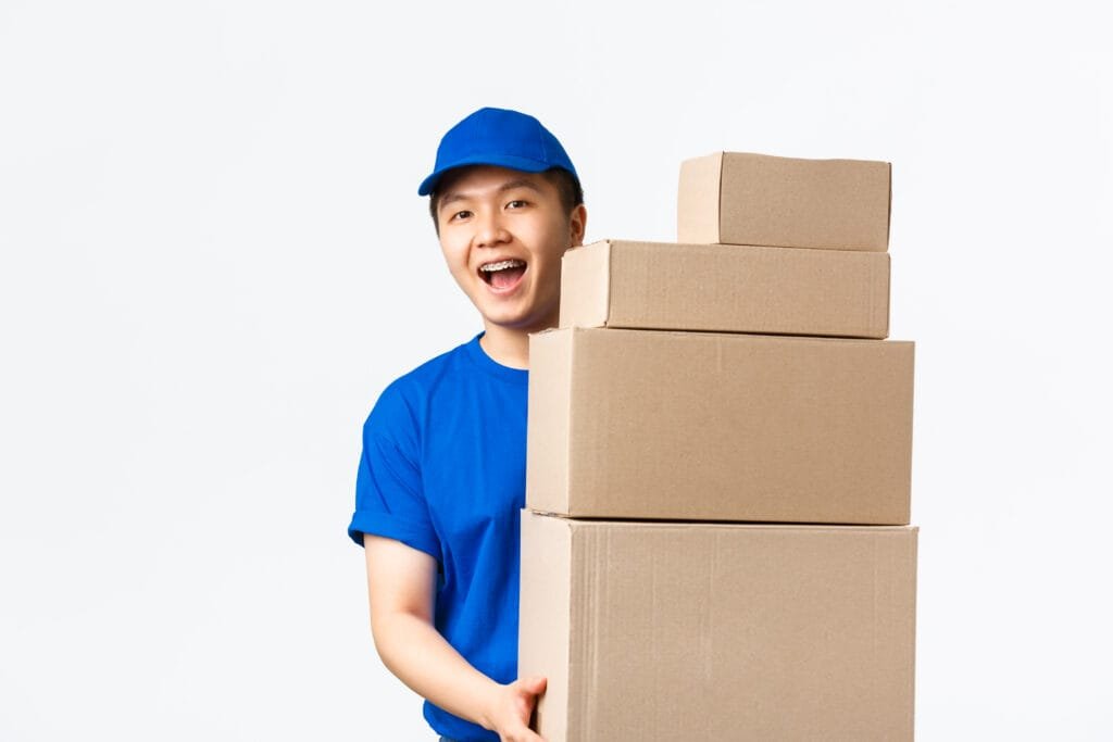 Online shopping, fast shipping concept. Friendly smiling young asian male courier in blue uniform carry boxes with orders. Delivery man bring parcels to your doorstep, standing white background